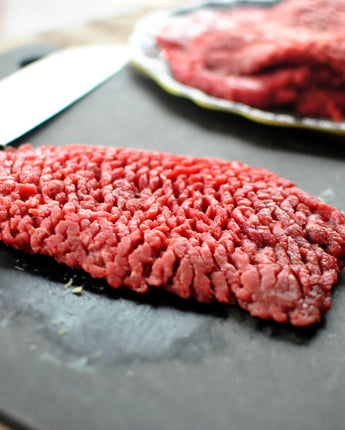 Raw cube steak on a stone next to plate of raw meats