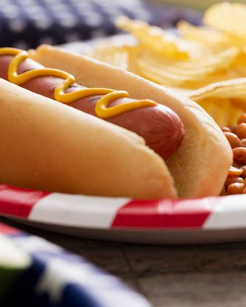 Grilled hot dog in a bun with mustard and sides of potato chips and baked beans