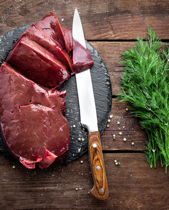 Raw sliced meat on a stone with a knife and garnishes