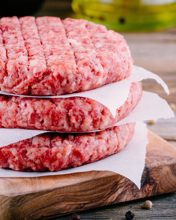 Raw stacked hamburger patties on a wooden cutting board