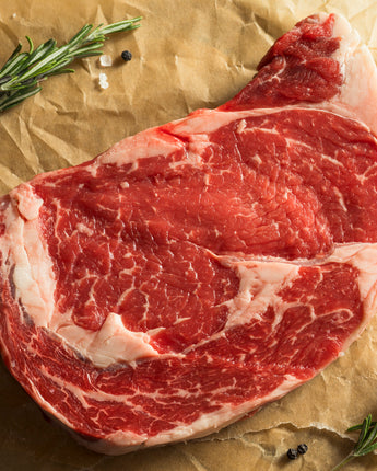 Raw steak on parchment paper with garnishes and spices