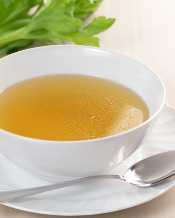 Cup of vegetable bouillon soup with a spoon and garnish